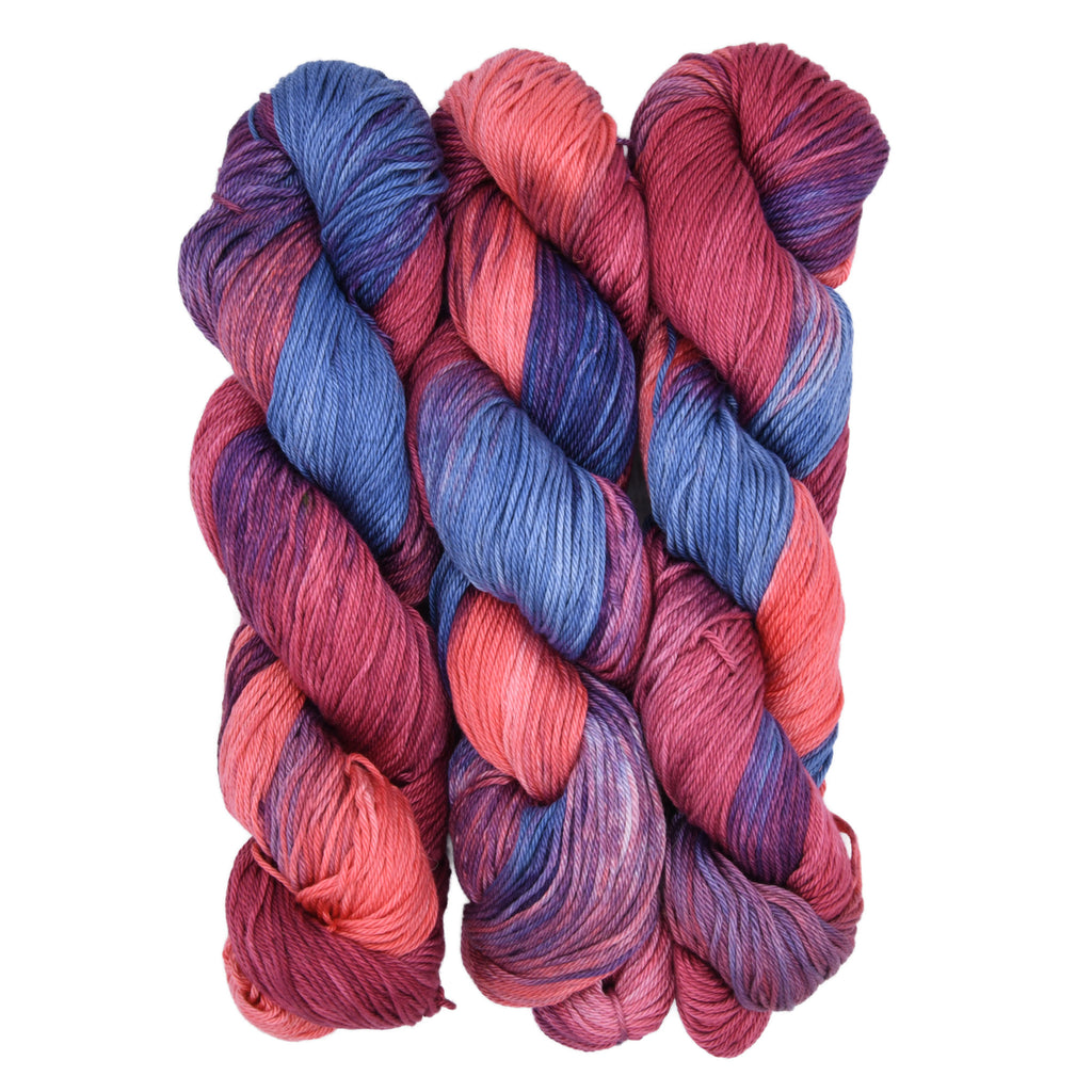 Three skeins of Woolly Headed Ideas Cotton DK weight hand-dyed yarn in colorway Bedtime Stories - a pink and blue variegated colorway on a white background