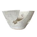 A handmade ceramic bowl with a unique asymmetrical split design, featuring a speckled off-white glaze with dark brown  flecks, set against a plain white background.