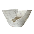 A handmade ceramic bowl with a unique asymmetrical split design, featuring a speckled off-white glaze with dark brown  flecks, set against a plain white background.