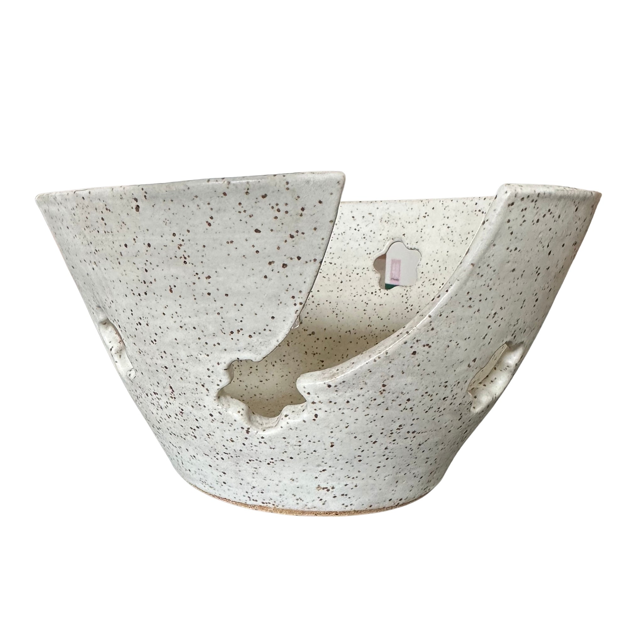 A handmade ceramic bowl with a unique asymmetrical split design, featuring a speckled off-white glaze with dark brown  flecks, set against a plain white background.