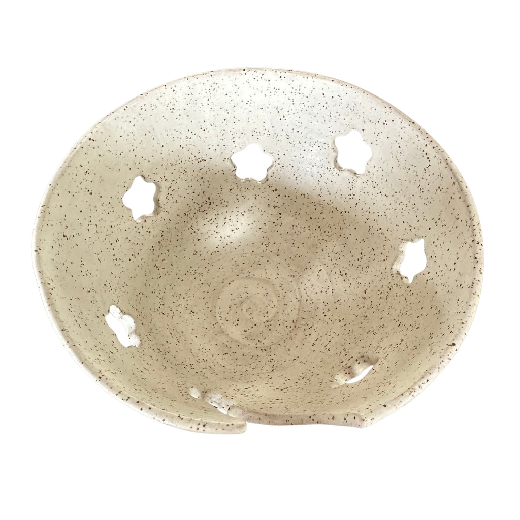 A handmade ceramic bowl with a speckled beige and white glaze, featuring five decorative cutouts on the inner rim, shown against a plain white background.