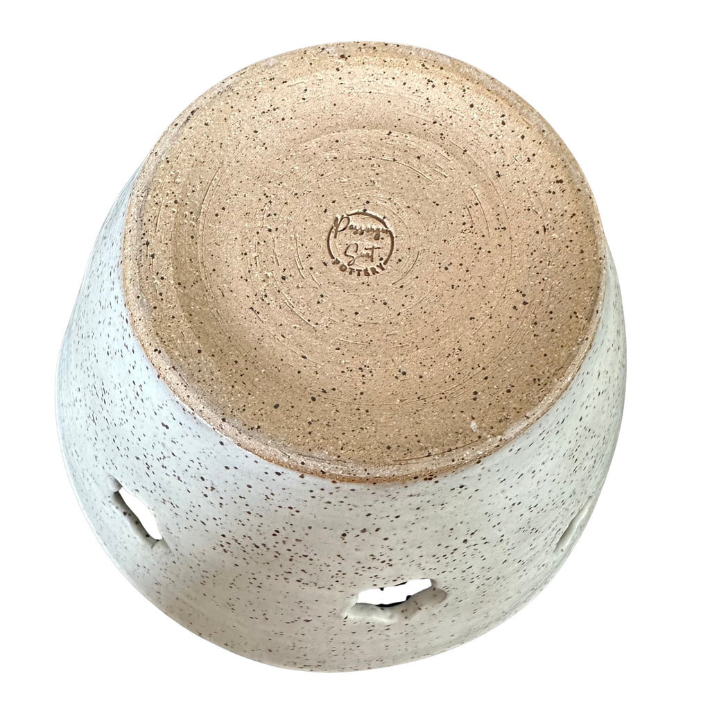 Bottom of a handmade ceramic yarn bowl from a top-down angle, featuring a speckled beige and white glaze with a natural brown clay bottom visible 
