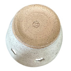 Bottom of a handmade ceramic yarn bowl from a top-down angle, featuring a speckled beige and white glaze with a natural brown clay bottom visible 