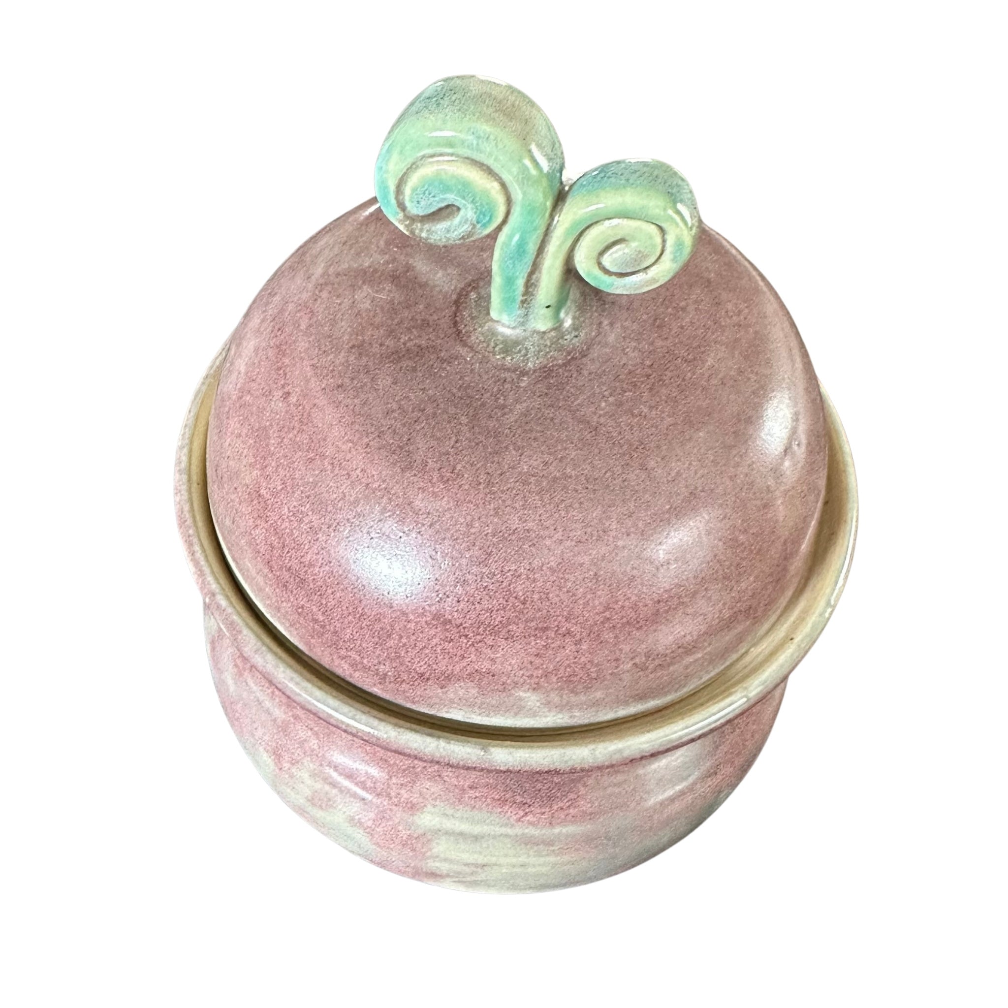 A small round ceramic lidded box with a dusty pink glaze and two sculpted mint-green handles on top, shown against a plain white background.